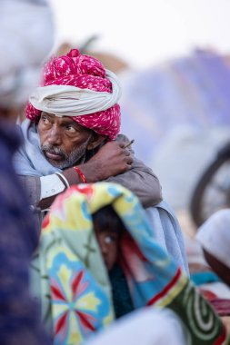 Puşkar, Rajasthan, Hindistan - Kasım 09 2024: Geleneksel beyaz giysili rajasthani erkek portresi çöl panayırında deve fuarı sırasında deve ticareti sırasında sarıklı.