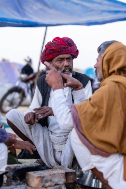 Puşkar, Rajasthan, Hindistan - Kasım 09 2024: Geleneksel beyaz giysili rajasthani erkek portresi çöl panayırında deve fuarı sırasında deve ticareti sırasında sarıklı.