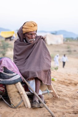 Puşkar, Rajasthan, Hindistan - Kasım 09 2024: Geleneksel beyaz giysili rajasthani erkek portresi çöl panayırında deve fuarı sırasında deve ticareti sırasında sarıklı.