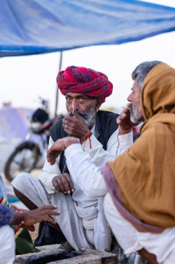 Puşkar, Rajasthan, Hindistan - Kasım 09 2024: Geleneksel beyaz giysili rajasthani erkek portresi çöl panayırında deve fuarı sırasında deve ticareti sırasında sarıklı.