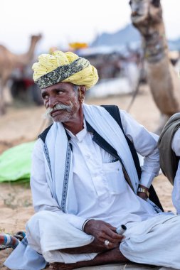 Puşkar, Rajasthan, Hindistan - Kasım 09 2024: Geleneksel giysili rajasthani erkek portresi çöl panayırında deve fuarı sırasında deve ticareti sırasında sarıklı.