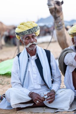 Puşkar, Rajasthan, Hindistan - Kasım 09 2024: Geleneksel giysili rajasthani erkek portresi çöl panayırında deve fuarı sırasında deve ticareti sırasında sarıklı.