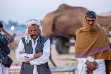 Puşkar, Rajasthan, Hindistan - Kasım 09 2024: Geleneksel giysili rajasthani erkek portresi çöl panayırında deve fuarı sırasında deve ticareti sırasında sarıklı.