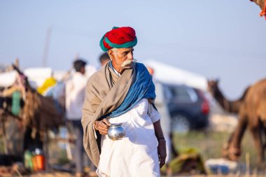 Puşkar, Rajasthan, Hindistan - Kasım 09 2024: Geleneksel giysili rajasthani erkek portresi çöl panayırında deve fuarı sırasında deve ticareti sırasında sarıklı.