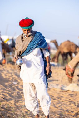 Puşkar, Rajasthan, Hindistan - Kasım 09 2024: Geleneksel giysili rajasthani erkek portresi çöl panayırında deve fuarı sırasında deve ticareti sırasında sarıklı.