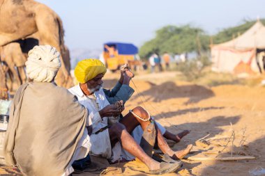 Puşkar, Rajasthan, Hindistan - Kasım 09 2024: Geleneksel giysili rajasthani erkek portresi çöl panayırında deve fuarı sırasında deve ticareti sırasında sarıklı.