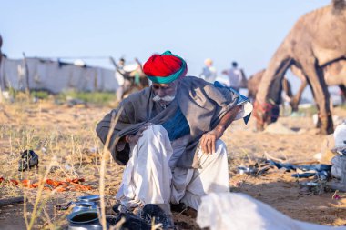 Puşkar, Rajasthan, Hindistan - Kasım 09 2024: Geleneksel giysili rajasthani erkek portresi çöl panayırında deve fuarı sırasında deve ticareti sırasında sarıklı.