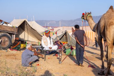 Puşkar, Rajasthan, Hindistan - Kasım 09 2024: Geleneksel giysili rajasthani erkek portresi çöl panayırında deve fuarı sırasında deve ticareti sırasında sarıklı.