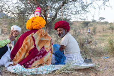 Puşkar, Rajasthan, Hindistan - Kasım 09 2024: Geleneksel beyaz giysili rajasthani erkek portresi çöl panayırında deve fuarı sırasında deve ticareti sırasında sarıklı.