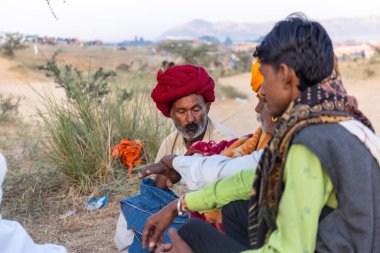 Puşkar, Rajasthan, Hindistan - Kasım 09 2024: Geleneksel beyaz giysili rajasthani erkek portresi çöl panayırında deve fuarı sırasında deve ticareti sırasında sarıklı.
