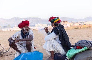 Puşkar, Rajasthan, Hindistan - Kasım 09 2024: Geleneksel beyaz giysili rajasthani erkek portresi çöl panayırında deve fuarı sırasında deve ticareti sırasında sarıklı.