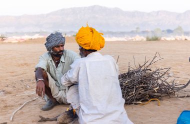 Puşkar, Rajasthan, Hindistan - Kasım 09 2024: Geleneksel beyaz giysili rajasthani erkek portresi çöl panayırında deve fuarı sırasında deve ticareti sırasında sarıklı.