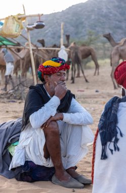 Puşkar, Rajasthan, Hindistan - Kasım 09 2024: Geleneksel giysili rajasthani erkek portresi çöl panayırında deve fuarı sırasında deve ticareti sırasında sarıklı.