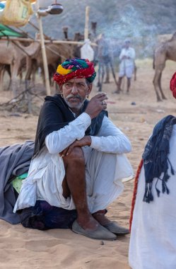 Puşkar, Rajasthan, Hindistan - Kasım 09 2024: Geleneksel giysili rajasthani erkek portresi çöl panayırında deve fuarı sırasında deve ticareti sırasında sarıklı.