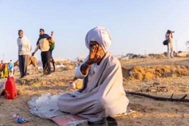 Puşkar, Rajasthan, Hindistan - Kasım 09 2024: Geleneksel beyaz giysili rajasthani erkek portresi çöl panayırında deve fuarı sırasında deve ticareti sırasında sarıklı.
