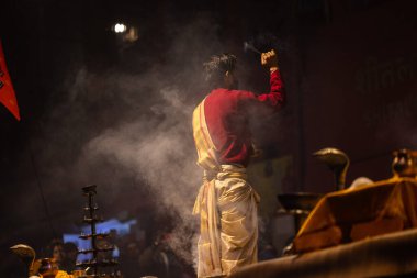 Varanasi, Uttar Pradesh, Hindistan - 20 Ocak 2024: Ganga aarti, Dashashwamedh ghat geleneksel elbise ve Hindu ayinleri ile kutsal nehir keneviri akşam ayini yapan genç bir rahibin portresi.