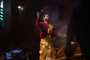 Varanasi, Uttar Pradesh, Hindistan - 20 Ocak 2024: Ganga aarti, Dashashwamedh ghat geleneksel elbise ve Hindu ayinleri ile kutsal nehir keneviri akşam ayini yapan genç bir rahibin portresi.
