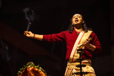 Varanasi, Uttar Pradesh, Hindistan - 20 Ocak 2024: Ganga aarti, Dashashwamedh ghat geleneksel elbise ve Hindu ayinleri ile kutsal nehir keneviri akşam ayini yapan genç bir rahibin portresi.