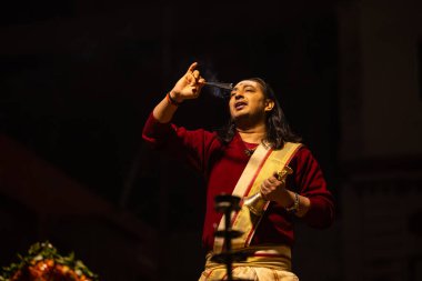 Varanasi, Uttar Pradesh, Hindistan - 20 Ocak 2024: Ganga aarti, Dashashwamedh ghat geleneksel elbise ve Hindu ayinleri ile kutsal nehir keneviri akşam ayini yapan genç bir rahibin portresi.