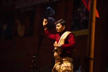 Varanasi, Uttar Pradesh, Hindistan - 20 Ocak 2024: Ganga aarti, Dashashwamedh ghat geleneksel elbise ve Hindu ayinleri ile kutsal nehir keneviri akşam ayini yapan genç bir rahibin portresi.