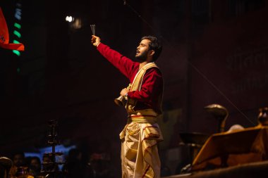 Varanasi, Uttar Pradesh, Hindistan - 20 Ocak 2024: Ganga aarti, Dashashwamedh ghat geleneksel elbise ve Hindu ayinleri ile kutsal nehir keneviri akşam ayini yapan genç bir rahibin portresi.