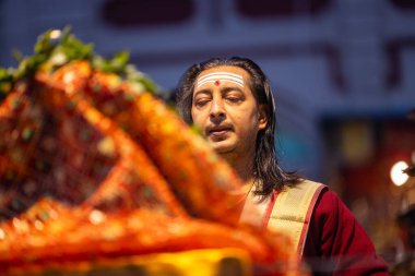 Varanasi, Uttar Pradesh, Hindistan - 20 Ocak 2024: Ganga aarti, Dashashwamedh ghat geleneksel elbise ve Hindu ayinleri ile kutsal nehir keneviri akşam ayini yapan genç bir rahibin portresi.