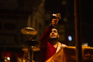 Varanasi, Uttar Pradesh, Hindistan - 20 Ocak 2024: Ganga aarti, Dashashwamedh ghat geleneksel elbise ve Hindu ayinleri ile kutsal nehir keneviri akşam ayini yapan genç bir rahibin portresi.
