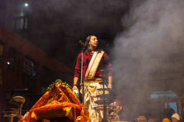 Varanasi, Uttar Pradesh, Hindistan - 20 Ocak 2024: Ganga aarti, Dashashwamedh ghat geleneksel elbise ve Hindu ayinleri ile kutsal nehir keneviri akşam ayini yapan genç bir rahibin portresi.