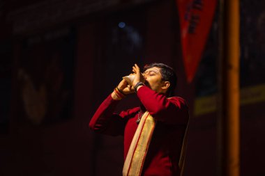 Varanasi, Uttar Pradesh, Hindistan - 20 Ocak 2024: Ganga aarti, Dashashwamedh ghat geleneksel elbise ve Hindu ayinleri ile kutsal nehir keneviri akşam ayini yapan genç bir rahibin portresi.