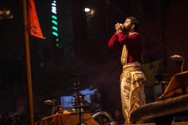 Varanasi, Uttar Pradesh, Hindistan - 20 Ocak 2024: Ganga aarti, Dashashwamedh ghat geleneksel elbise ve Hindu ayinleri ile kutsal nehir keneviri akşam ayini yapan genç bir rahibin portresi.
