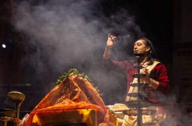 Varanasi, Uttar Pradesh, Hindistan - 20 Ocak 2024: Ganga aarti, Dashashwamedh ghat geleneksel elbise ve Hindu ayinleri ile kutsal nehir keneviri akşam ayini yapan genç bir rahibin portresi.