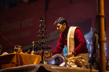 Varanasi, Uttar Pradesh, Hindistan - 20 Ocak 2024: Ganga aarti, Dashashwamedh ghat geleneksel elbise ve Hindu ayinleri ile kutsal nehir keneviri akşam ayini yapan genç bir rahibin portresi.