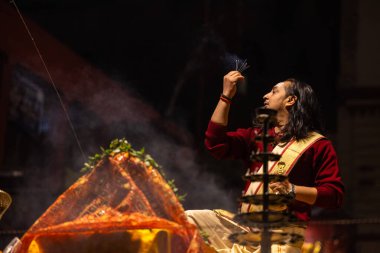 Varanasi, Uttar Pradesh, Hindistan - 20 Ocak 2024: Ganga aarti, Dashashwamedh ghat geleneksel elbise ve Hindu ayinleri ile kutsal nehir keneviri akşam ayini yapan genç bir rahibin portresi.