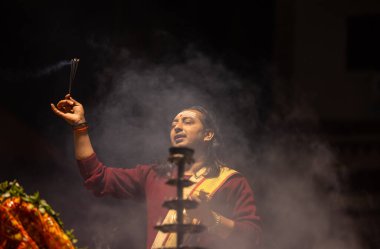 Varanasi, Uttar Pradesh, Hindistan - 20 Ocak 2024: Ganga aarti, Dashashwamedh ghat geleneksel elbise ve Hindu ayinleri ile kutsal nehir keneviri akşam ayini yapan genç bir rahibin portresi.