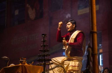 Varanasi, Uttar Pradesh, Hindistan - 20 Ocak 2024: Ganga aarti, Dashashwamedh ghat geleneksel elbise ve Hindu ayinleri ile kutsal nehir keneviri akşam ayini yapan genç bir rahibin portresi.