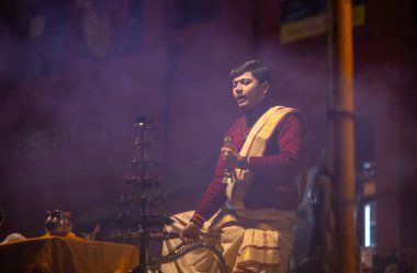 Varanasi, Uttar Pradesh, Hindistan - 20 Ocak 2024: Ganga aarti, Dashashwamedh ghat geleneksel elbise ve Hindu ayinleri ile kutsal nehir keneviri akşam ayini yapan genç bir rahibin portresi.