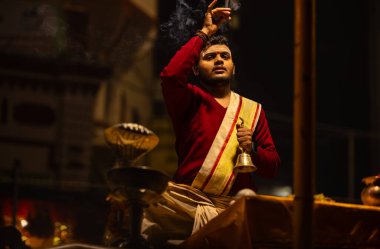 Varanasi, Uttar Pradesh, Hindistan - 20 Ocak 2024: Ganga aarti, Dashashwamedh ghat geleneksel elbise ve Hindu ayinleri ile kutsal nehir keneviri akşam ayini yapan genç bir rahibin portresi.