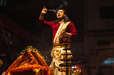 Varanasi, Uttar Pradesh, Hindistan - 20 Ocak 2024: Ganga aarti, Dashashwamedh ghat geleneksel elbise ve Hindu ayinleri ile kutsal nehir keneviri akşam ayini yapan genç bir rahibin portresi.