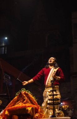 Varanasi, Uttar Pradesh, Hindistan - 20 Ocak 2024: Ganga aarti, Dashashwamedh ghat geleneksel elbise ve Hindu ayinleri ile kutsal nehir keneviri akşam ayini yapan genç bir rahibin portresi.