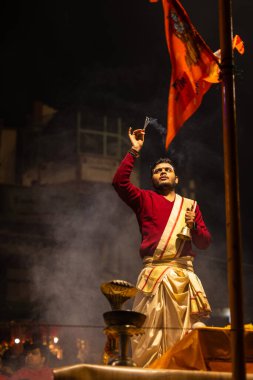 Varanasi, Uttar Pradesh, Hindistan - 20 Ocak 2024: Ganga aarti, Dashashwamedh ghat geleneksel elbise ve Hindu ayinleri ile kutsal nehir keneviri akşam ayini yapan genç bir rahibin portresi.