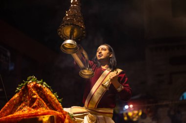 Varanasi, Uttar Pradesh, Hindistan - 20 Ocak 2024: Ganga aarti, Dashashwamedh ghat geleneksel elbise ve Hindu ayinleri ile kutsal nehir keneviri akşam ayini yapan genç bir rahibin portresi.