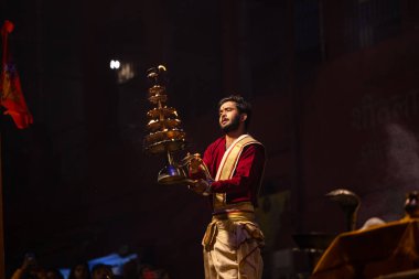 Varanasi, Uttar Pradesh, Hindistan - 20 Ocak 2024: Ganga aarti, Dashashwamedh ghat geleneksel elbise ve Hindu ayinleri ile kutsal nehir keneviri akşam ayini yapan genç bir rahibin portresi.