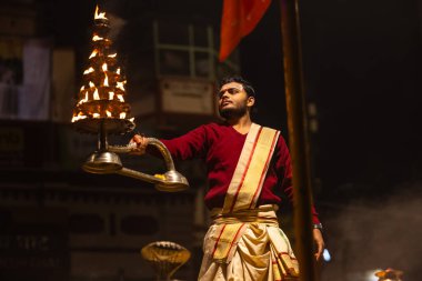 Varanasi, Uttar Pradesh, Hindistan - 20 Ocak 2024: Ganga aarti, Dashashwamedh ghat geleneksel elbise ve Hindu ayinleri ile kutsal nehir keneviri akşam ayini yapan genç bir rahibin portresi.