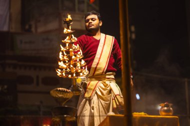 Varanasi, Uttar Pradesh, Hindistan - 20 Ocak 2024: Ganga aarti, Dashashwamedh ghat geleneksel elbise ve Hindu ayinleri ile kutsal nehir keneviri akşam ayini yapan genç bir rahibin portresi.