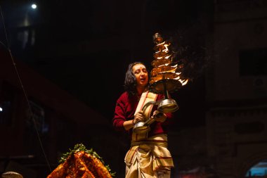 Varanasi, Uttar Pradesh, Hindistan - 20 Ocak 2024: Ganga aarti, Dashashwamedh ghat geleneksel elbise ve Hindu ayinleri ile kutsal nehir keneviri akşam ayini yapan genç bir rahibin portresi.