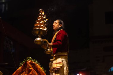 Varanasi, Uttar Pradesh, Hindistan - 20 Ocak 2024: Ganga aarti, Dashashwamedh ghat geleneksel elbise ve Hindu ayinleri ile kutsal nehir keneviri akşam ayini yapan genç bir rahibin portresi.