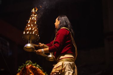 Varanasi, Uttar Pradesh, Hindistan - 20 Ocak 2024: Ganga aarti, Dashashwamedh ghat geleneksel elbise ve Hindu ayinleri ile kutsal nehir keneviri akşam ayini yapan genç bir rahibin portresi.