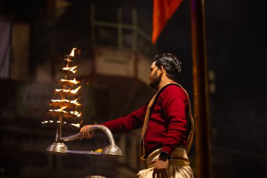Varanasi, Uttar Pradesh, Hindistan - 20 Ocak 2024: Ganga aarti, Dashashwamedh ghat geleneksel elbise ve Hindu ayinleri ile kutsal nehir keneviri akşam ayini yapan genç bir rahibin portresi.