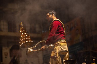 Varanasi, Uttar Pradesh, Hindistan - 20 Ocak 2024: Ganga aarti, Dashashwamedh ghat geleneksel elbise ve Hindu ayinleri ile kutsal nehir keneviri akşam ayini yapan genç bir rahibin portresi.