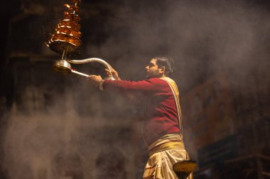 Varanasi, Uttar Pradesh, Hindistan - 20 Ocak 2024: Ganga aarti, Dashashwamedh ghat geleneksel elbise ve Hindu ayinleri ile kutsal nehir keneviri akşam ayini yapan genç bir rahibin portresi.